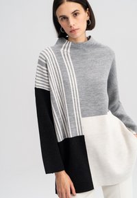 Grijze en zwarte oversize trui met een hoge nek, voorzien van gestreepte patronen en een kleurblokontwerp. Gemaakt van een zacht breimateriaal.