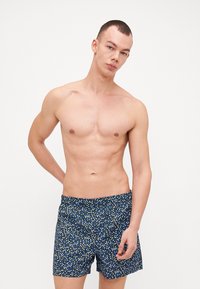 Shorts de bain bleu marine avec un motif à pois multicolores. Tissu léger, longueur mi-cuisse, taille élastique sans matériel visible.