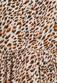 Tessuto beige con stampa leopardata irregolare nera e arancione, caratterizzato da una fila verticale di bottoni bianchi e una cucitura arricciata sotto la vita.