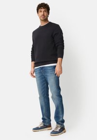 Sweat-shirt col rond marine, jean bleu clair et baskets bleues avec accents beige. Coupe décontractée et poignets côtelés sur le sweat-shirt.