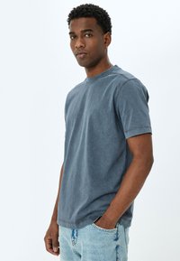 Kortärmad t-shirt med rund halsringning i blekt blått bomull. Har en avslappnad passform, lätt textur och sömnadsdetaljer längs halsringningen och ärmarna.