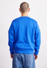Blå sweatshirt med rund hals och ribbade muddar. Materialet är mjukt och har en enkel design. Kombineras med ljusblå denimshorts.