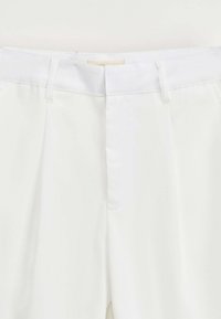 Pantalons blancs ajustés en tissu lisse, avec un devant plat et une taille épurée avec passants de ceinture ; sans poches ni motifs visibles.