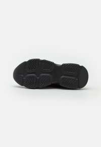 Semelle de chaussure noire en caoutchouc texturé avec des motifs en zigzag pour une meilleure adhérence. Bout arrondi et talon solide pour la stabilité.