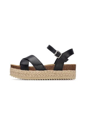 Sandalias cuña de cuero negro con diseño de tiras cruzadas, base de corcho y entresuela tejida similar al yute; correa ajustable en el tobillo con hebilla metálica.