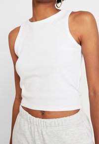 Vit ribbad tanktop med rund halsringning och ärmlös design, med en kort längd och en slät textur.