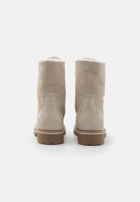 Botines beige hechos de suave ante, con suela de goma, punta redonda y forro de piel visible en la parte superior, con detalles de costura.