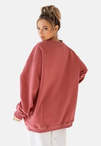 Przesadny, długorękawowy sweatshirt w odcieniu przykurzonego różu, wykonany z miękkiego materiału, z okrągłym dekoltem oraz ściągaczami na rękawach i dole.