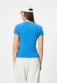 Farkku, lyhythihainen t-paita voimakkaan sinisessä puuvillassa, jolla on sileä rakenne. Varustettu pyöreällä kaula-aukolla ja yksinkertaisella helma. Yhdistetty valkoisiin housuihin.