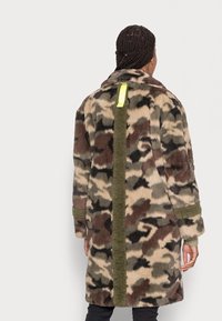 Płaszcz polarowy z wzorem kamuflażowym w odcieniach zieleni, brązu i beżu. Z żółtym akcentem z tyłu i fakturowanymi rękawami.