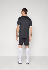 Zwart sportshirt met witte accenten, gecombineerd met bijpassende shorts. Inclusief kniehoge witte sokken en voetbalschoenen. Soepele stoftextuur.