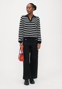 Svart-hvit stripete genser med V-hals og ribbestrikkede mansjetter, kombinert med svart vide jeans og en liten rød håndveske. Sorte klumpete sko.