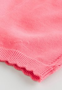 Rózsaszín kötött anyag, texturált felülettel és fodros széllel. Az anyag lágy és könnyű, enyhe redőkben elrendezve.