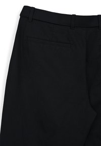 Pantaloni neri con una texture liscia, frontale piatto e tasca posteriore. La cintura presenta passanti per la cintura per un tocco di dettagli in più.
