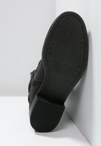Bota de cuero negro con suela de goma. Presenta una superficie texturizada y un tacón ligeramente elevado. Talla marcada como 36.