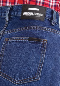 Vaqueros de mezclilla con un acabado azul profundo, que presentan un bolsillo trasero y una etiqueta negra que dice "DRDENIM JEANMAKERS" en texto blanco.