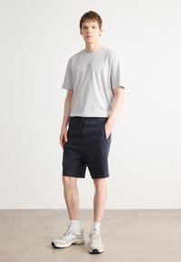Ljust grå kortärmad t-shirt med broderad logotyp, i kombination med mörkblå shorts med justerbart snöre och sidoficka. Vita sneakers.