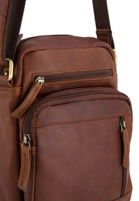 Braune Ledertasche mit zwei Reißverschlussfächern, einer strukturierten Oberfläche, kontrastierenden Nähten und Metallakzenten.