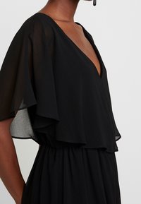 Black dress featuring a deep V-neck and flowing sheer sleeves. The fabric is smooth with a gathered waist for a loose fit.
