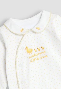 Bodysuit blanc à manches longues avec un motif d'étoiles jaunes, des bordures dorées, une broderie de canard et le texte "bienvenue petit bout" près du bas.