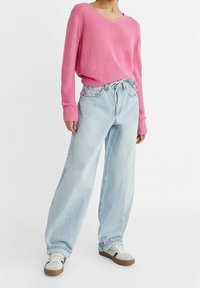 Pull rose côtelé à col en V, associé à un jean taille haute à jambes larges bleu clair, complété par des baskets blanches aux semelles marron.