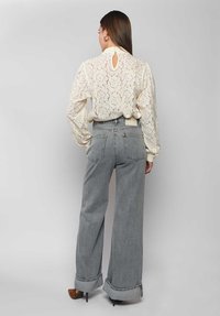 Spitzenbluse mit Ballonärmeln in Cremefarbe, mit einem Schlüsselloch-Detail im Rücken; kombiniert mit hoch taillierten, weit geschnittenen grauen Jeans.