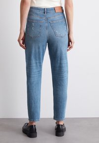 Ljusblå denimjeans med en avslappnad passform, featuring en medelhög midja, två bakfickor och slitna detaljer. Bärs med svarta skor.