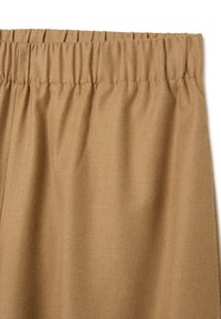 Ceinture élastique avec texture froncée, fabriquée en tissu doux couleur beige. Surface lisse avec un léger éclat.