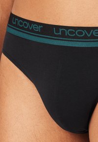 Czarny bokser wykonany z gładkiego materiału. Posiada ciemnozielony pas z nadrukiem słowa "odkryj" w powtarzającym się wzorze oraz dopasowany krój.