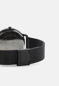 Ceas de mână din plasă neagră cu carcasă din oțel inoxidabil, având un cadran rotund și închidere cu clemă, cu un design elegant și modern.