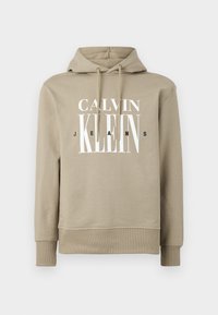Sudadera con capucha beige, hecha de una tela suave, presenta un gráfico frontal con "CALVIN KLEIN JEANS" en letras en negrita blancas y negras.