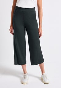 Mörkgrå vida byxor i mjukt tyg, med hög midja och en slät yta. Bärs med vita sneakers för kontrast.