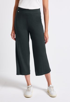 Pantaloni larghi grigio scuro realizzati in tessuto morbido, con vita alta e una texture liscia. Indossati con sneakers bianche per un contrasto.