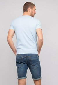 T-shirt bleu clair à manches courtes avec un design ajusté, associé à un short en jean foncé avec ourlets roulés et poches arrière.