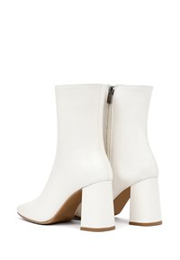 Bottines blanches en cuir avec un bout pointu et un talon carré. Elles présentent une fermeture éclair latérale et une texture lisse avec des accents de couture minimalistes.