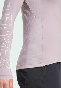 Maglietta atletica a manica lunga viola chiaro con un motivo testurizzato, caratterizzata da un grande logo bianco "TERREX" sulla manica sinistra.