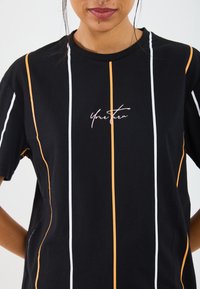 Svart t-shirt med kort ärm och vita samt orangea vertikala ränder. Har texten "Your Turn" i kursiv på framsidan. Mjuk bomullstyg.