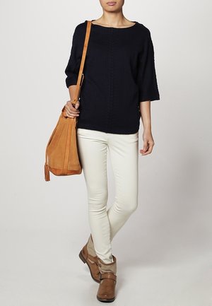 Navy knitted sweater, loose fit, round neckline; cream skinny jeans; brown ankle boots; tan suede shoulder bag with fringe detail.