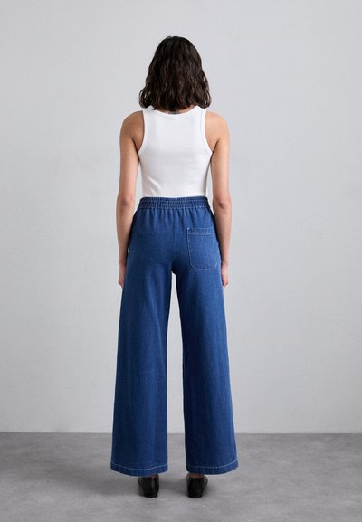 Niebieskie dżinsy w szerokim kroju wykonane z denimu, z elastycznym pasem, jedną tylną kieszenią i gładką teksturą, w połączeniu z białym topem na ramiączkach.
