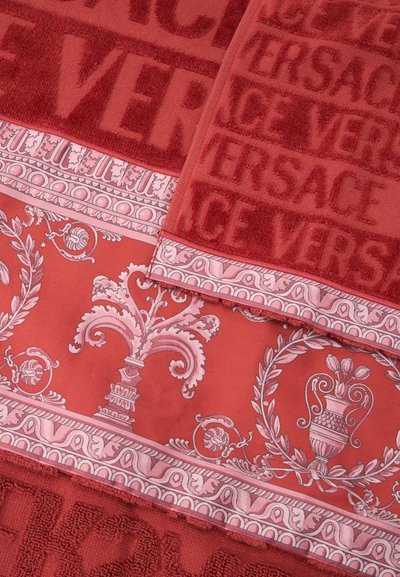 Κόκκινες πετσέτες με ανάγλυφο κείμενο «VERSACE» και διακοσμητικό ροζ μπαρόκ πλαίσιο με μοτίβα από έλικες, φύλλα και αγγεία.