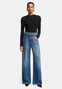 Maglietta nera a maniche lunghe con texture a coste, abbinata a jeans in denim blu a gamba larga con vita cinturata e colore sbiadito.
