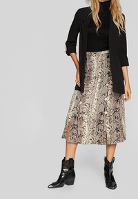 Slangeskinds midi-skjørt i beige og brunt med frontslids og knapper. Sammen med en sort turtleneck og en struktureret blazer, suppleret med sorte ankelstøvler.