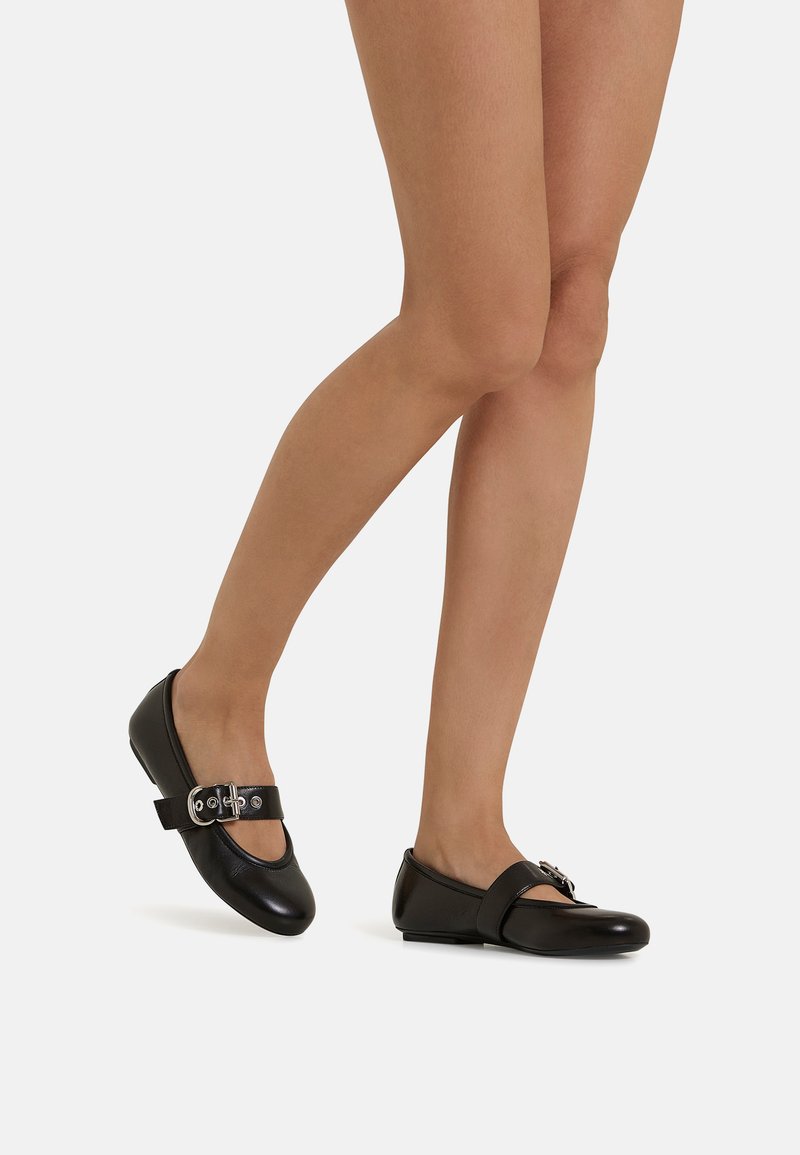 Ballerine in pelle nera con punta arrotondata, caratterizzate da un dettaglio con fibbia e una fascia sul dorso del piede; texture liscia e design minimalista.