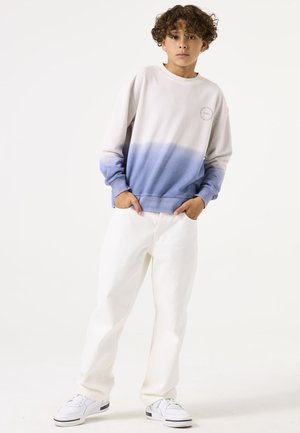 Sudadera con degradado de luz que va de gris claro a azul, con cuello redondo y puños acanalados, combinada con vaqueros blancos y zapatillas.