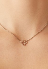 Zilveren ketting met een bloemenvormige hanger met uitsparingen, rustend op een gladde huid. Eenvoudig ontwerp, lichtgewicht.