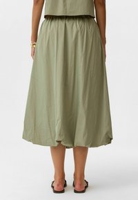 Groene, lichte, knie-lange rok met een geplooide taille en een gebogen zoom, gemaakt van een gladde stof. Draag het met platte sandalen.