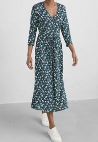 Mekko, jossa on pitkä ja kukallinen kuvio, tummansininen pohjaväri vihreillä ja purppuran sävyisillä kuvioilla, V-pääntie, kolme neljänneksen mittaiset hihat, vyötärö korostettu ja liehuva helma. Yhdistetty valkoisiin tennareihin.