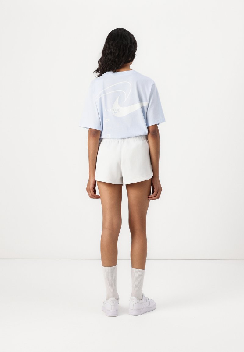 Camiseta de manga corta azul claro con un diseño de olas blancas en la parte trasera, combinada con pantalones cortos y calcetines blancos. Estilo minimalista y casual.