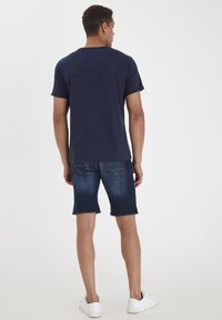 Temno modra bombažna majica s kratkimi rokavi, v kombinaciji z denim kratkimi hlačami s posvetljeno opravo in zavihanimi robovi, dopolnjena z belimi superge.