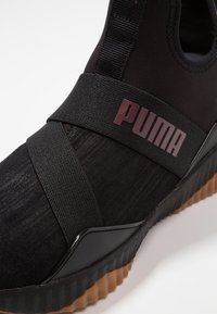Svarta slip-on Puma sneakers med korsade elastiska band, strukturerad ovandel och detaljerad gummisula.
